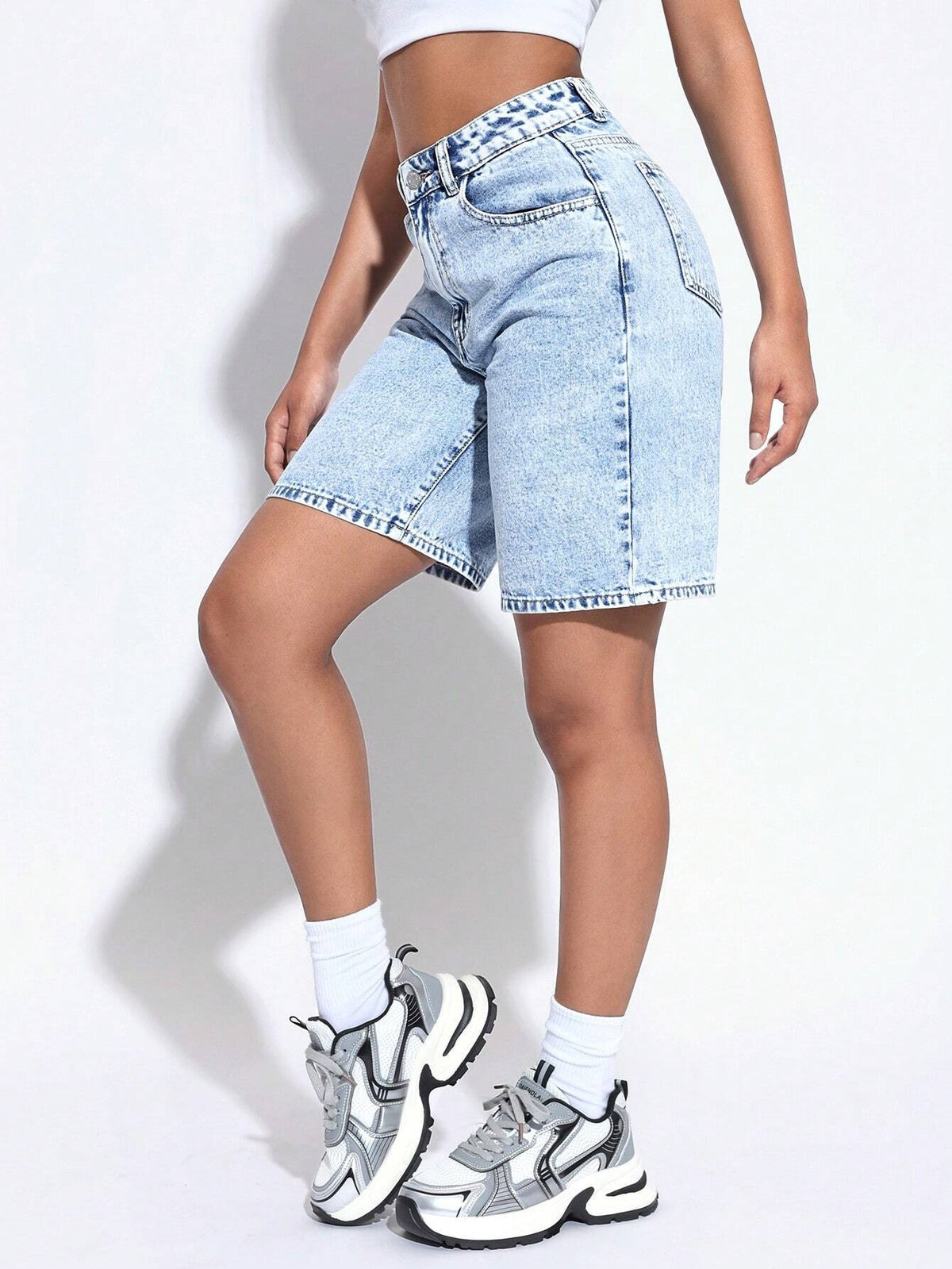 Person wearing light blue denim shorts and white sneakers on a plain background