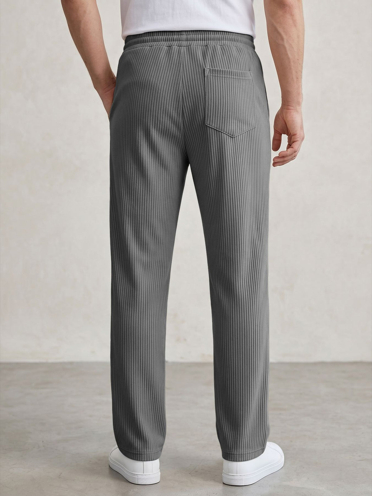 A person shown from the back wearing gray pinstriped trousers, a white t-shirt, and white sneakers against a neutral studio backdrop.