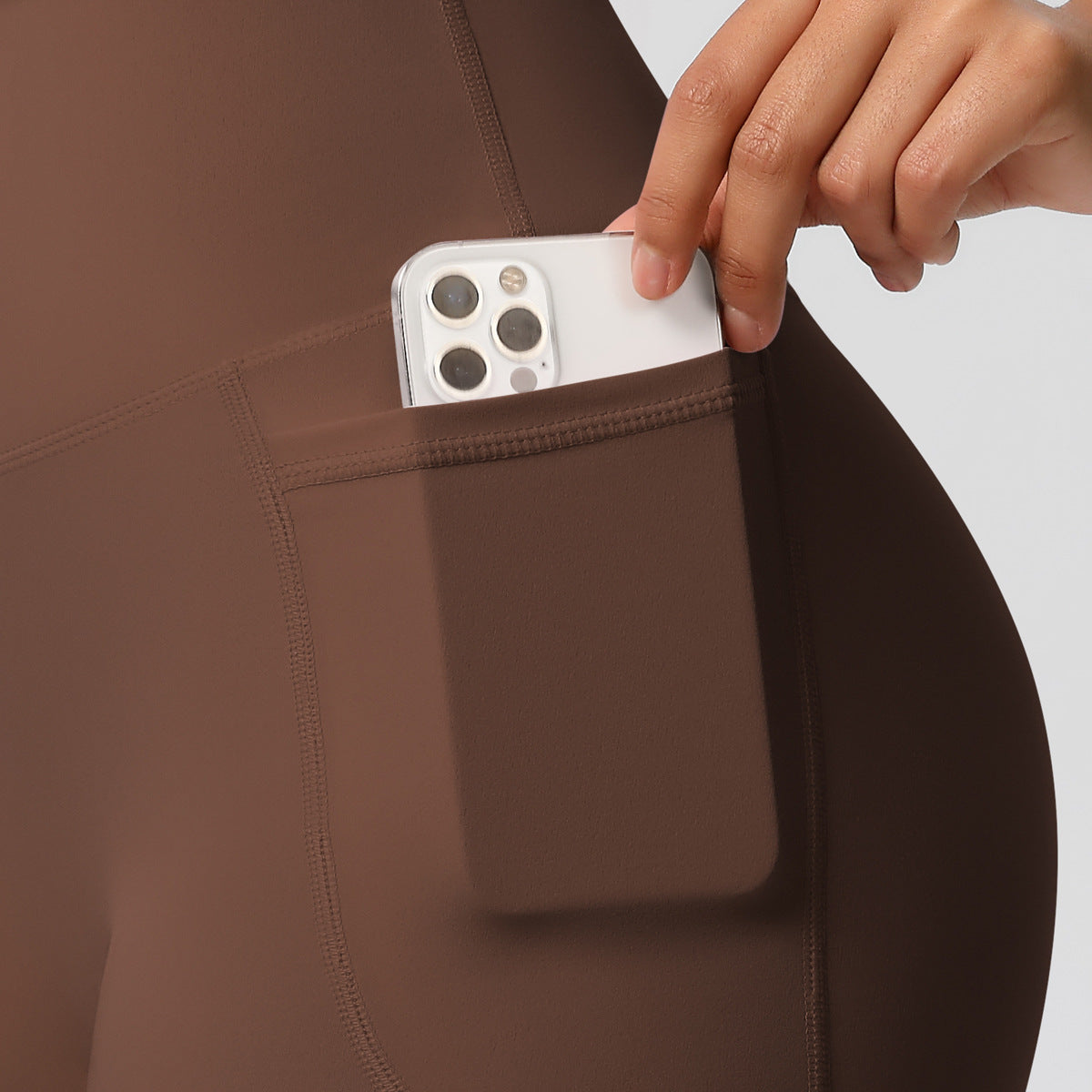 Person placing a smartphone into a pocket of brown pants against a neutral background