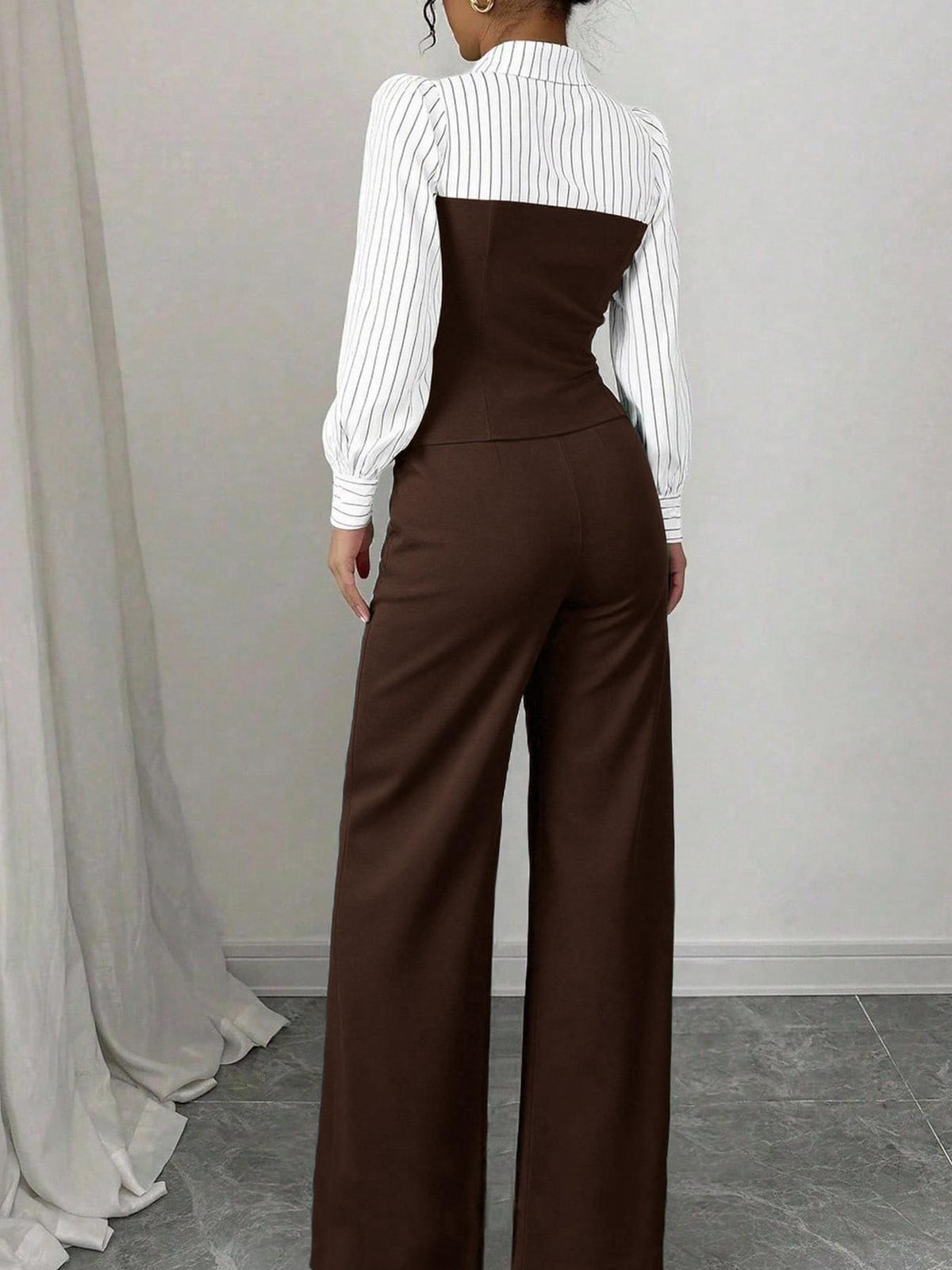 Person wearing a white blouse with a high collar and brown wide-leg pants against a plain background.