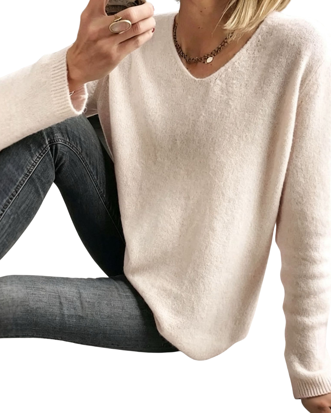 A woman wearing a cream-colored V-neck knit sweater and dark gray jeans, shown in a cropped mirror selfie style against a white background.