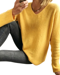 A woman wearing a fuzzy mustard yellow V-neck sweater and dark gray jeans, cropped from the mouth down against a plain white background.