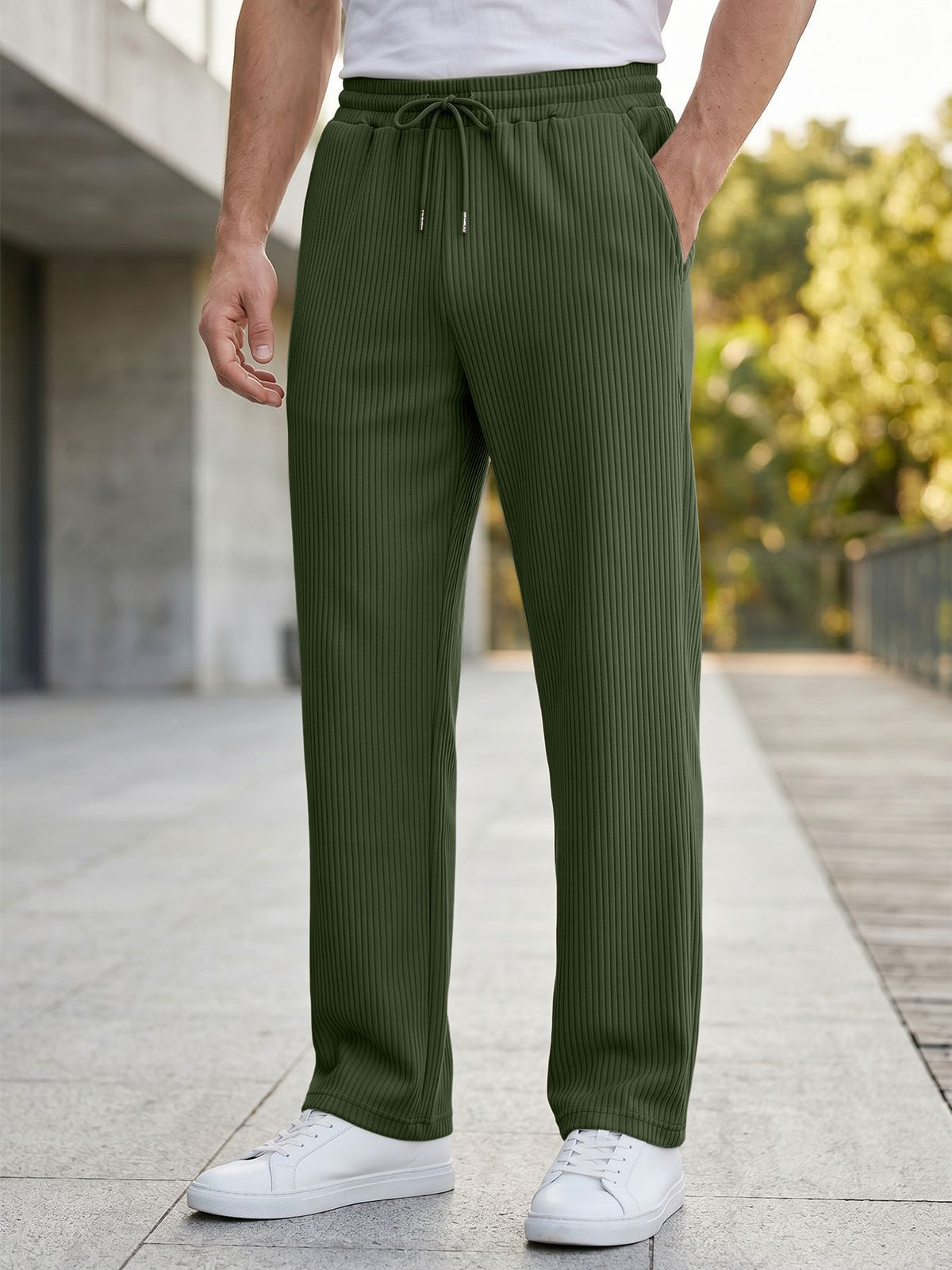 A person wearing dark charcoal gray pinstriped drawstring trousers, styled with a white t-shirt and white sneakers, standing on a paved outdoor walkway.