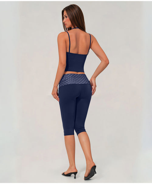 A woman shown from the back wearing a navy blue activewear set consisting of a spaghetti-strap crop top and matching high-waisted capri leggings with a patterned waistband, paired with black heels against a light gray studio background.