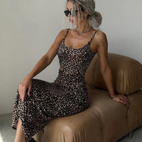 Woman in a leopard print dress sitting on a brown couch against a plain wall.