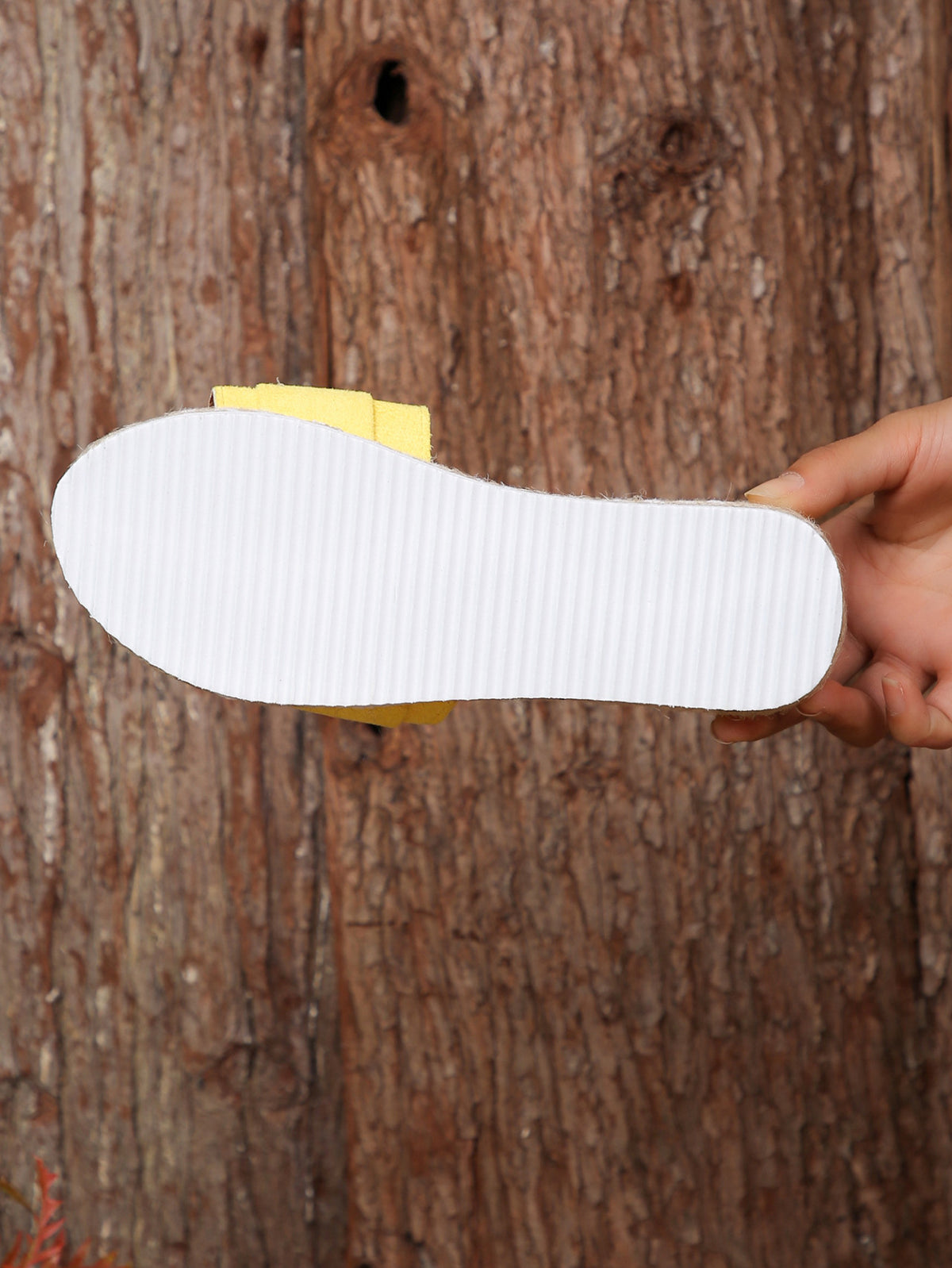 A white textured shoe insole held horizontally by a hand against a rustic brown tree bark background.