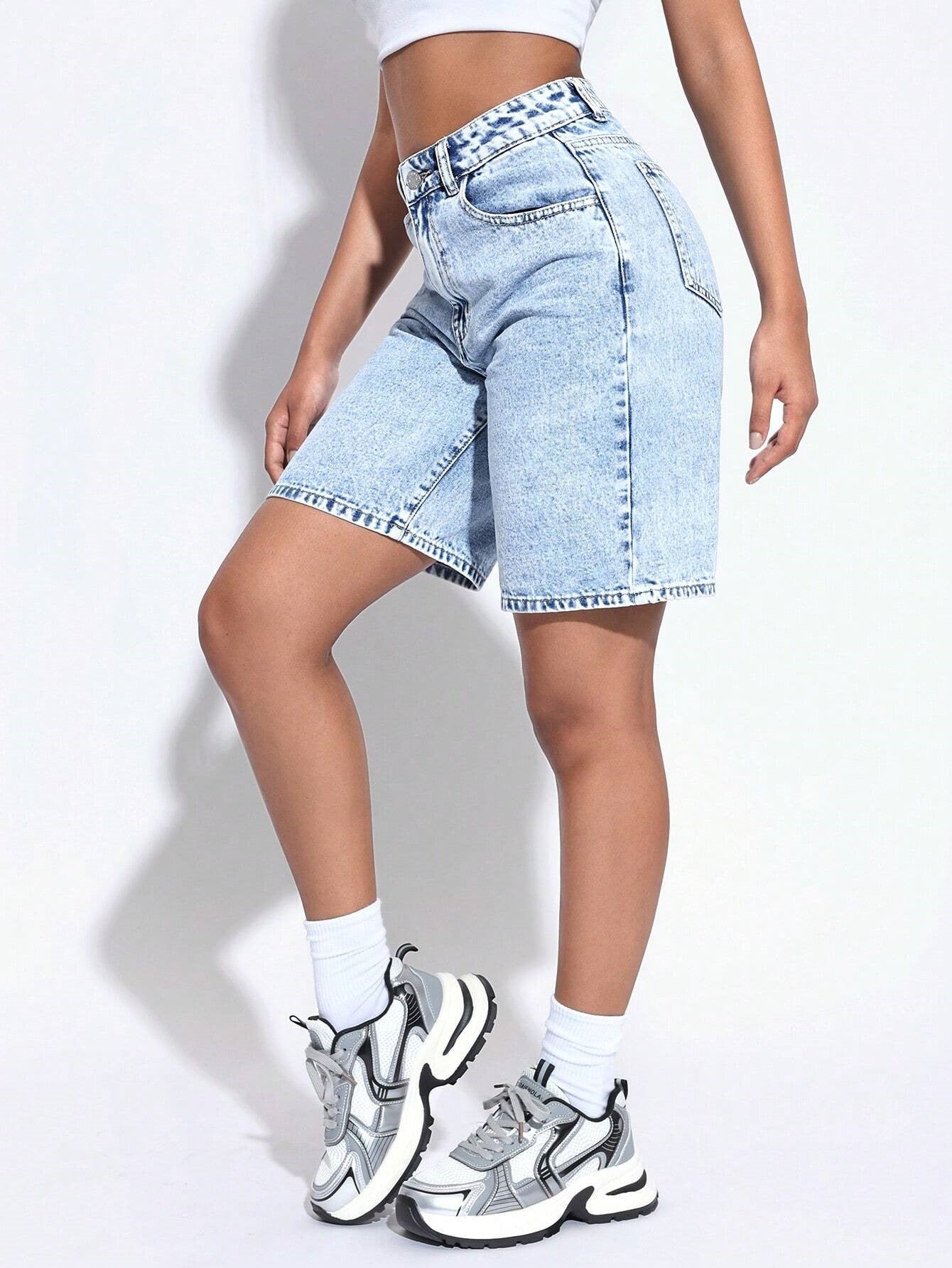 Person wearing light blue denim shorts and white sneakers on a plain background