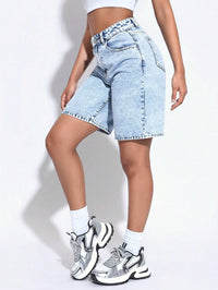 Person wearing light blue denim shorts and white sneakers on a plain background