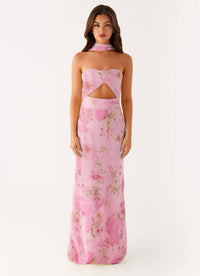A woman modeling a pink strapless maxi dress with a floral print and a cutout at the waist, set against a plain white studio background.