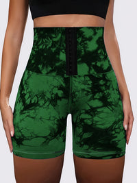 Green tie-dye high-waisted athletic shorts with a black lace-up front, shown on a model against a light gray background.
