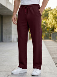 A person wearing burgundy ribbed drawstring lounge pants, a white t-shirt, and white sneakers, standing on a paved outdoor walkway.