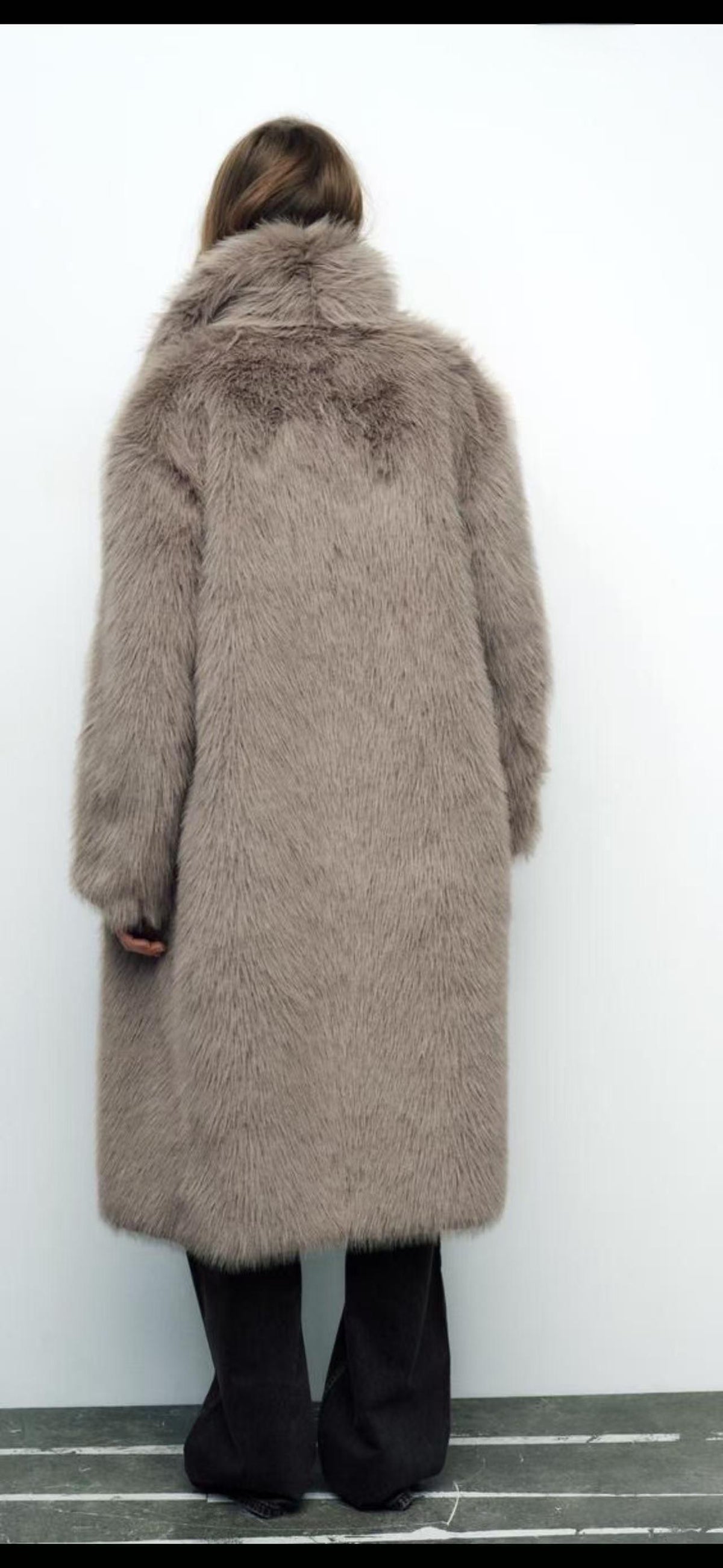 Person wearing a long, fluffy coat with a fur-lined hood against a white background