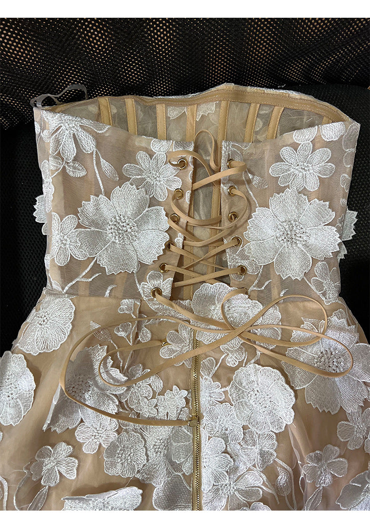 A close-up of a beige and white floral lace dress featuring a corset-style bodice with tan elastic laces and a front zipper.