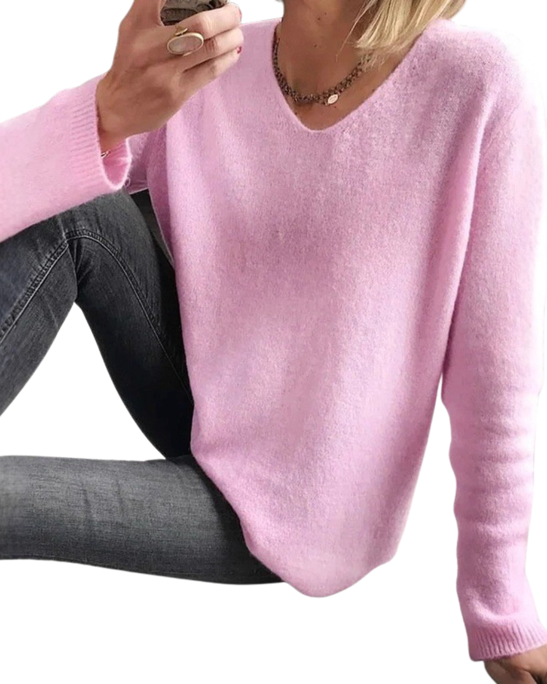 A woman wearing a light pink long-sleeve V-neck knit sweater and dark gray jeans, cropped from the chest down against a plain white background.