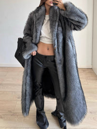 Person wearing a long gray fur coat with a plain background