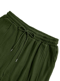 Close-up of olive green pleated pants showing the elastic drawstring waistband and ribbed fabric texture against a white background.