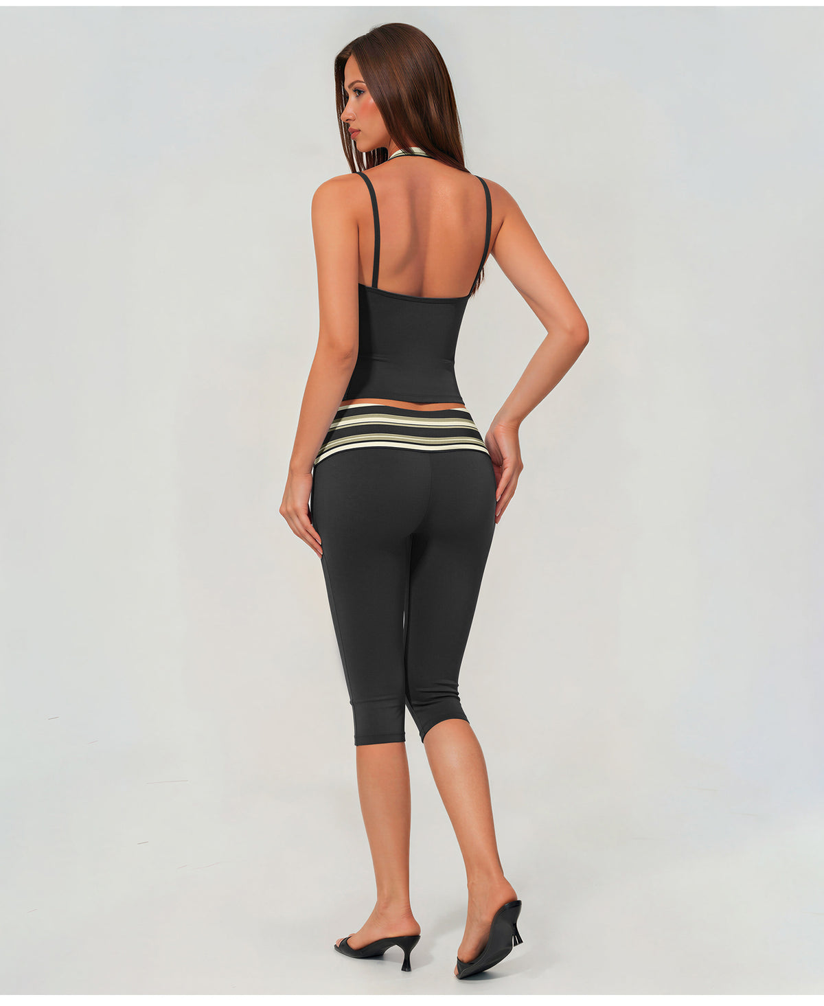A woman shown from the back wearing a black two-piece activewear set consisting of a spaghetti-strap tank top and matching capri leggings with a horizontal striped waistband.