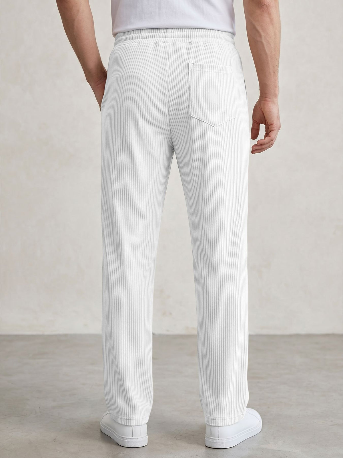 White ribbed knit trousers shown from the back on a model, featuring an elastic waistband, side pockets, and a relaxed straight-leg fit.