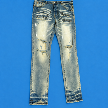 Distressed light-wash blue jeans with heavy fading, whiskering, and ripped details on the thighs and legs, laid flat against a solid blue background.