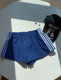 A pair of royal blue athletic shorts with white side stripes, laid flat on a white circular table next to a black baseball cap.