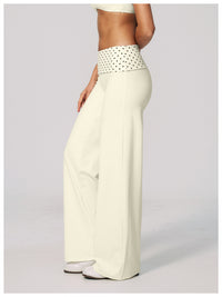 A model is shown from the waist down wearing high-waisted, wide-leg pants in cream with a contrasting white waistband featuring black polka dots.