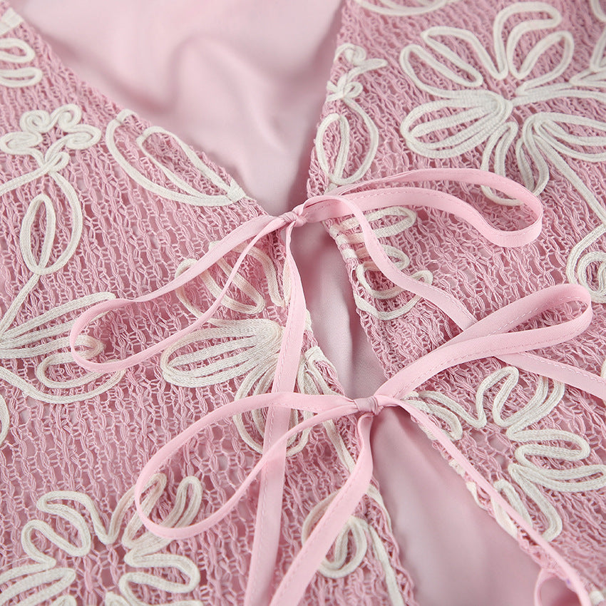 Close-up of a pink lace garment with white floral embroidery and a matching pink satin ribbon tied in the center.