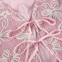 Close-up of a pink lace garment with white floral embroidery and a matching pink satin ribbon tied in the center.