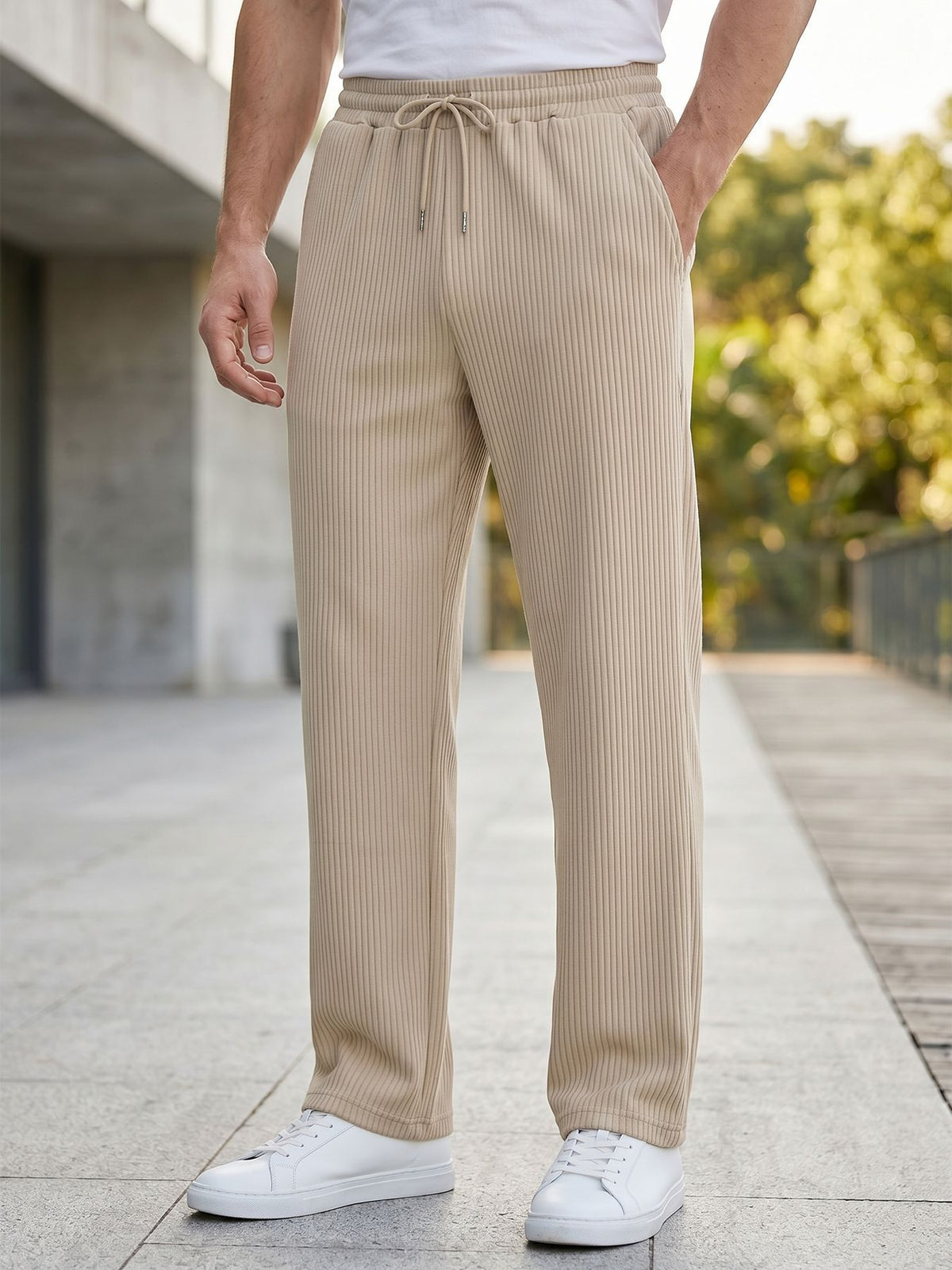 A person wearing beige ribbed drawstring trousers with a white t-shirt and white sneakers, standing outdoors on a paved walkway.