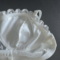 White lace bra cup with satin-like fabric and scalloped lace trim, photographed close up on a dark textured surface.