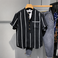 A men's short-sleeve button-front shirt with vertical white stripes on a black base, hanging on a wooden hanger next to gray jeans on a clothing rack.