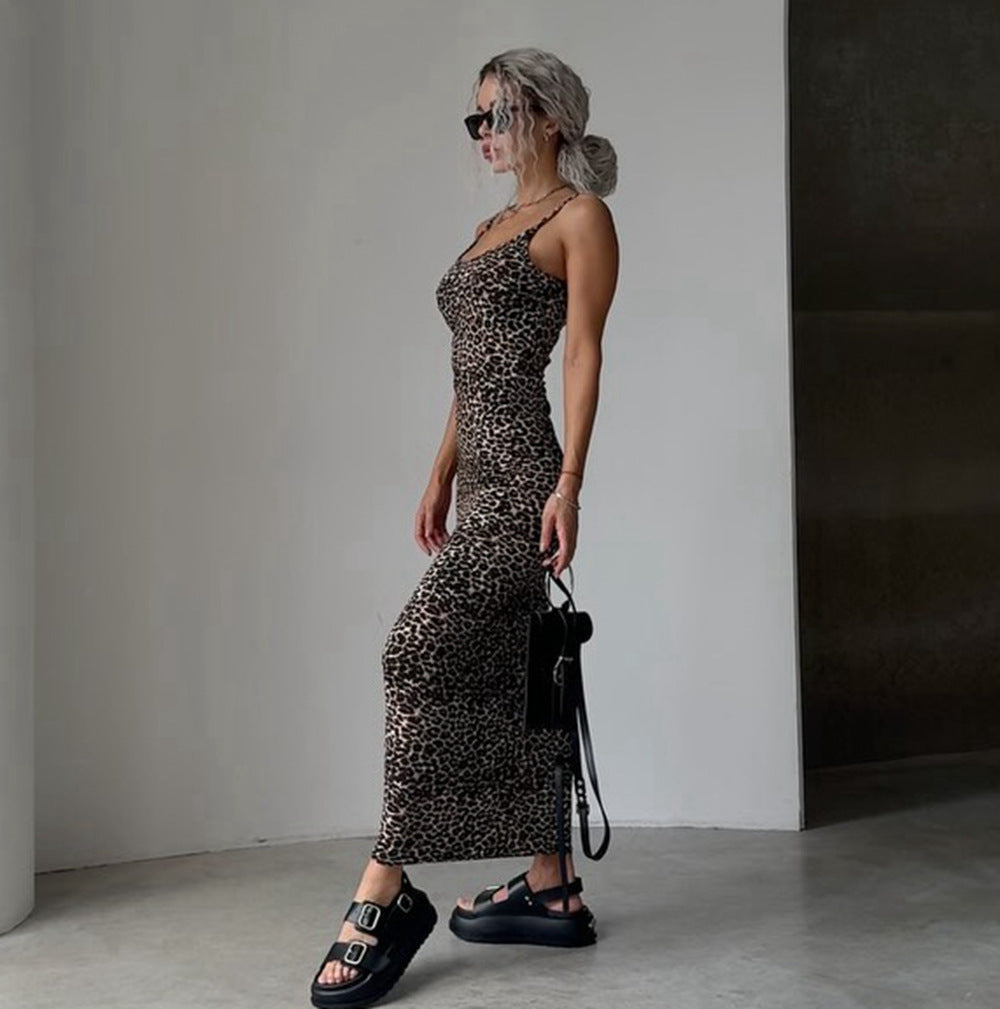 A woman wearing a sleeveless leopard-print maxi dress, black platform sandals, and sunglasses, holding a small black handbag in a minimalist indoor setting.