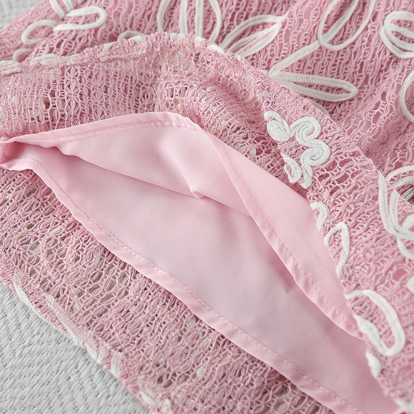 Close-up of a pink lace fabric with white embroidered floral patterns and a matching pink satin inner lining.