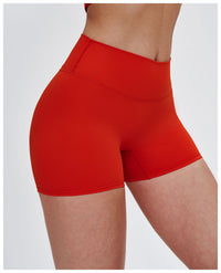 A close-up side view of a model wearing bright red high-waisted athletic shorts against a light gray studio background.