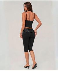 A woman shown from the back wearing a black two-piece activewear set consisting of a spaghetti-strap crop top and high-waisted capri leggings with a sheer mesh waistband.