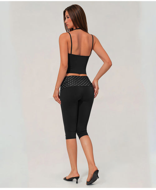 A woman shown from the back wearing a black two-piece activewear set consisting of a spaghetti-strap crop top and high-waisted capri leggings with a sheer mesh waistband.