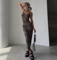 A woman modeling a fitted leopard-print camisole and matching leggings set, standing in a minimalist white room and holding a black handbag.