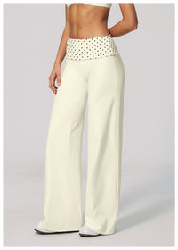 A model wearing high-waisted, wide-leg pants in cream with a white waistband covered in small black polka dots, shown from the torso down against a light gray studio background.