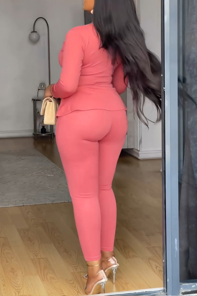 Woman in a pink outfit standing in a room with wooden flooring.