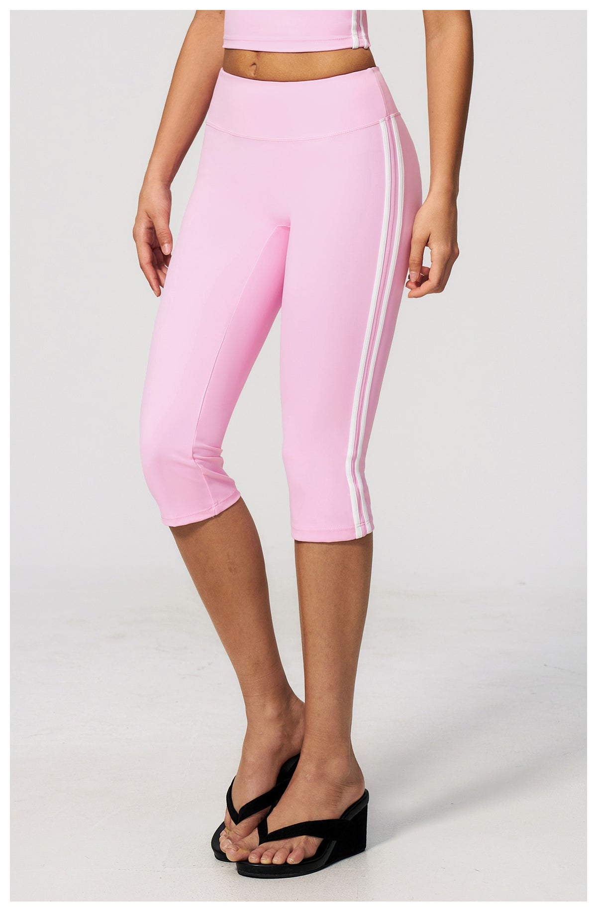 Pink capri leggings with white stripes worn by a person on a light gray background