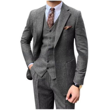 A man wearing a slim-fit three-piece gray tweed suit with a matching vest and trousers, styled with a white dress shirt, a brown paisley tie, and a matching pocket square, set against a plain white background.