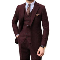 A men's three-piece suit in a deep burgundy or maroon textured fabric, featuring a jacket, matching vest, and trousers, styled with a white dress shirt, a brown paisley tie, and a matching pocket square on a white background.