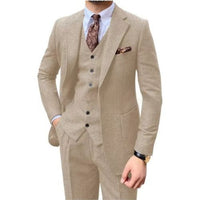 A man wearing a beige three-piece suit with a matching vest and trousers, styled with a white dress shirt, a brown patterned tie, and a matching pocket square, against a plain white background.