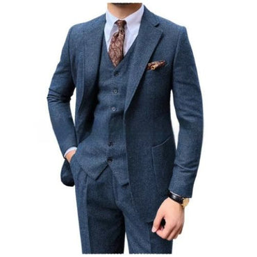 A man wearing a three-piece blue textured suit with a white dress shirt, a brown paisley tie, and a matching pocket square, shown against a plain white background.